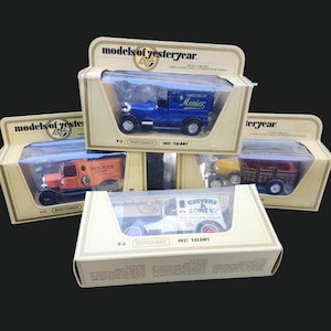 May include: Several vintage toy trucks in their original packaging are displayed. The trucks are in various colors, including blue, orange, and white, and are labeled with the "models of yesteryear" brand. The packaging is tan with clear plastic windows.
