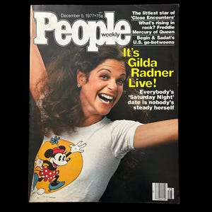 May include: People Weekly magazine cover from December 5, 1977, featuring Gilda Radner. Radner is smiling and wearing a white t-shirt with a Minnie Mouse graphic. The cover includes text about 'Saturday Night' and other articles.