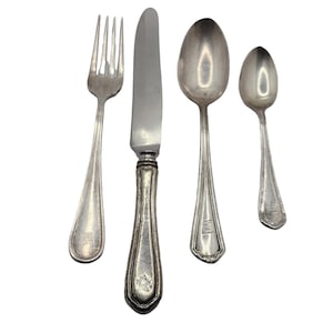 May include: A set of four antique silver-colored utensils: a fork, a knife, a large spoon, and a small spoon. The knife has a decorative handle. Each piece has a unique design and appears to be vintage silverware.