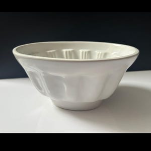May include: A white ceramic bowl with a fluted exterior and a rounded rim. The bowl has a pedestal base and is likely used for serving or baking. The bowl's dimensions are not visible in the image.