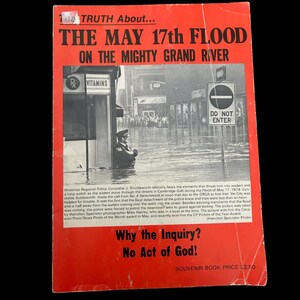 May include: A vintage souvenir book with a red cover, featuring the title "THE MAY 17th FLOOD ON THE MIGHTY GRAND RIVER." The cover includes a black and white photo of a flooded street scene with a police officer. Text includes "Why the Inquiry? No Act of God!"
