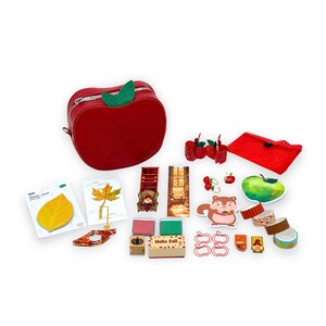 May include: A collection of fall-themed stationery and accessories. Includes a red apple-shaped bag, stickers, washi tape, stamps, and decorative paper clips. The items feature autumn leaves, apples, and a squirrel. The phrase "Hello Fall" is visible on a wooden block.