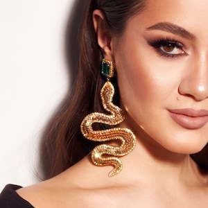 Peut inclure: Une femme portant un haut noir à épaules dénudées avec des boucles d'oreilles en forme de serpent dorées avec des accents verts.