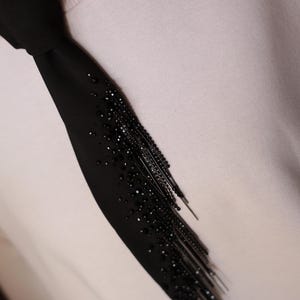 Puede incluir: Una corbata negra con una franja de cuentas y lentejuelas negras.