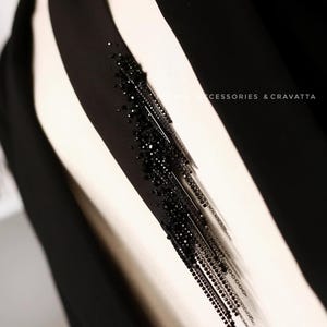 Puede incluir: Una corbata negra con un detalle de flecos de cuentas. El fleco est&aacute; hecho de peque&ntilde;as cuentas negras y cadenas met&aacute;licas. El texto "FROMLI_ACCESSORIES & CRAVATTA" es visible en la parte inferior de la imagen.