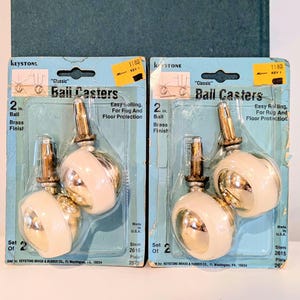 May include: Two sets of "Classic" ball casters, each containing two pieces. The casters are 2 inches in diameter with a brass finish and a white, rounded ball. The packaging includes text that reads "Easy Rolling, For Rug And Floor Protection."
