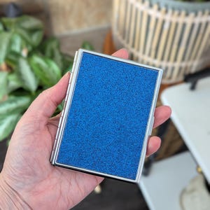 May include: A set of three ceramic mugs with a speckled, matte finish. The mugs are in shades of cream, light gray, and dark gray. Each mug has a simple, minimalist design and a rounded handle.