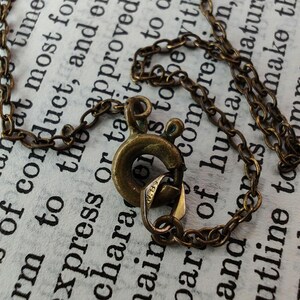 Puede incluir: Primer plano de un collar de cadena de lat&oacute;n con un cierre de langosta. La cadena est&aacute; hecha de peque&ntilde;os anillos unidos. El cierre es un dise&ntilde;o simple y funcional.