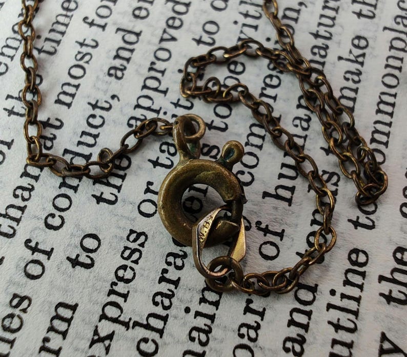 Puede incluir: Primer plano de un collar de cadena de lat&oacute;n con un cierre de langosta. La cadena est&aacute; hecha de peque&ntilde;os anillos unidos. El cierre es un dise&ntilde;o simple y funcional.