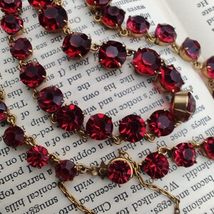 May include: A vintage red rhinestone necklace with gold chain links. The necklace is laying on a book with text.
