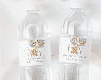 May include: Two clear water bottles with labels that read "It's a Boy" with a teddy bear and balloons. The bottles are on a white, decorative plate with a ribbon.