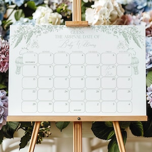 May include: A white calendar with a floral border and the text "Guess the arrival date of Baby Williams" on a wooden easel surrounded by blue, pink, and white hydrangeas.