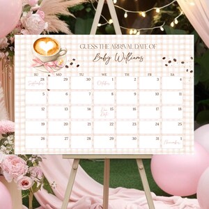May include: A baby shower calendar on a wooden easel, with the text "GUESS THE ARRIVAL DATE OF Baby Williams". The calendar has a coffee cup graphic and a pink and tan checkered background. Pink balloons and floral arrangements decorate the background.