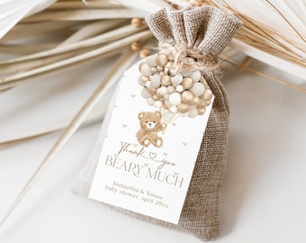 Puede incluir: Una etiqueta blanca de agradecimiento con un oso de peluche marrón que sostiene globos. La etiqueta dice "Muchas gracias, osito" y "Samantha & Tomas Baby Shower, abril 2023". La etiqueta está atada a una pequeña bolsa de arpillera.