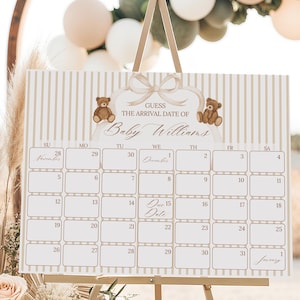 May include: A baby shower calendar sign on a gold easel. The sign has a beige striped background with the text "GUESS THE ARRIVAL DATE OF Baby Williams". Two teddy bear illustrations are at the top.