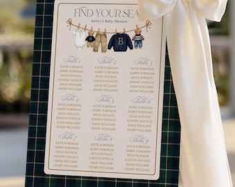 May include: A seating chart for Avery's Baby Shower, displayed on a gold easel. The chart has a dark green plaid border and features a clothesline with baby clothes and teddy bears. A large white bow adorns the side.