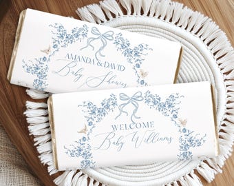 Puede incluir: Dos envoltorios de barra de chocolate blanco con diseños florales azules y detalles dorados. El envoltorio superior dice "Amanda & David Baby Shower" y el envoltorio inferior dice "Bienvenido Bebé Williams".