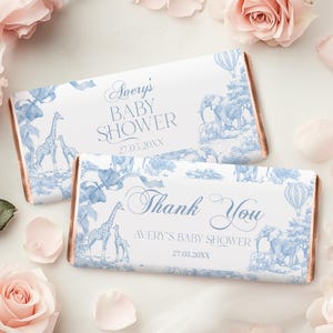 May include: Two blue and white chocolate bar wrappers with a safari animal theme. The top wrapper says "Avery's Baby Shower 27.03.20XX". The bottom wrapper says "Thank You Avery's Baby Shower 27.03.20XX".