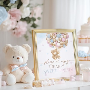 May include: A gold framed sign with a teddy bear holding balloons in blue, pink, and gold colors. The sign says "Please enjoy Bear-y Sweet Treats".