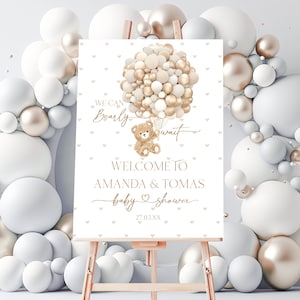Peut inclure: Une pancarte d'accueil blanche avec des lettres dorées et un ours en peluche tenant des ballons. La pancarte indique "We can barely wait. Welcome to Amanda & Tomas baby shower. 27.03.XX".