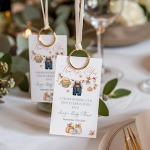 Może przedstawiać: Dwie karty z podziękowaniami na baby shower ze złotymi uchwytami na pierścionki. Karty mają motyw dyni z tekstem "Thank You" i "For Showering Our Little Pumpkin With Love!" Na kartach wydrukowano również datę "September 27th 2025".