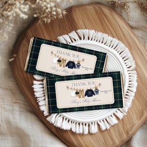 Op de afbeelding: Twee chocoladereepverpakkingen met een groen geruit patroon. Elke verpakking heeft een label met de tekst "THANK YOU" en "Avery's Baby Shower". De labels bevatten illustraties van babykleding en een teddybeer.