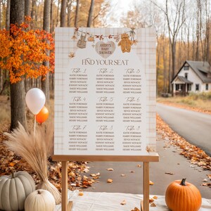 May include: A wooden seating chart for a baby shower, with the text "Avery's Baby Shower" and "Find Your Seat." The chart is decorated with fall-themed elements and displayed outdoors with pumpkins and balloons.