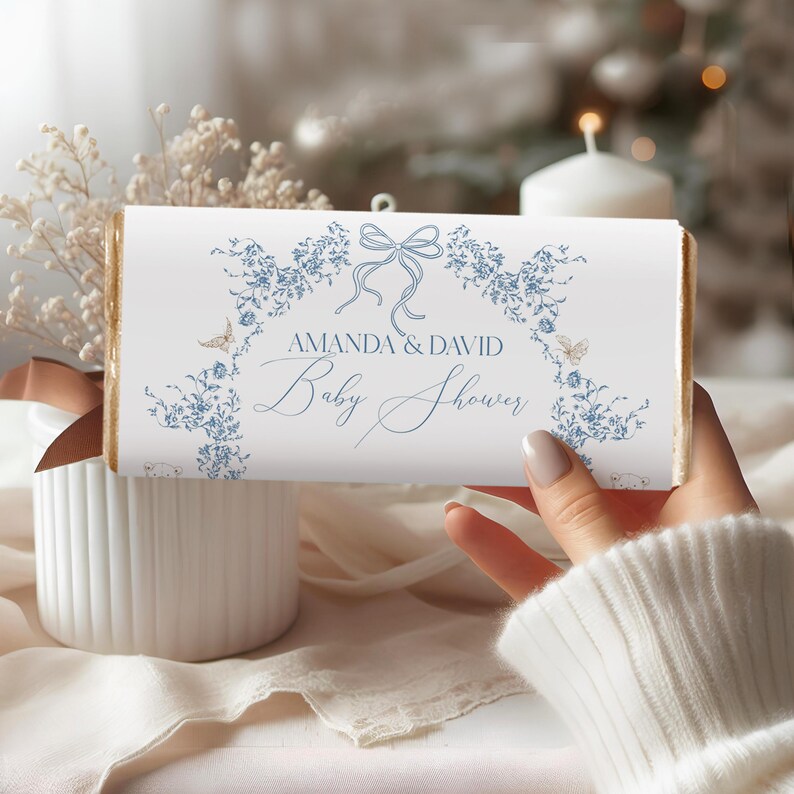 May include: White chocolate bar wrapper with a blue floral design and gold accents. The text reads "Amanda & David Baby Shower".