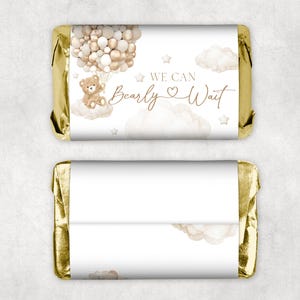 Pode incluir: Embrulho de barra de chocolate dourado e branco com um urso de pelúcia segurando balões e o texto "We can bearly wait".