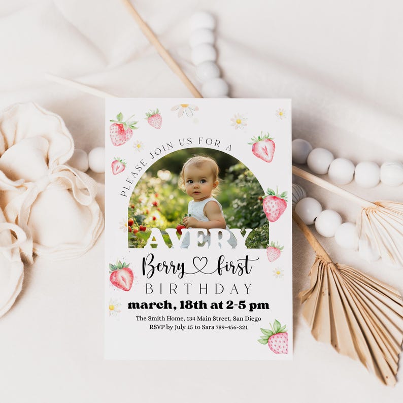 May include: A white invitation card with a photo of a baby, strawberries, and daisies. The text reads "Avery Berry first birthday" and includes the date, time, and location. The card is decorated with strawberry and daisy illustrations.