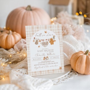May include: A baby shower invitation with a fall theme. The invitation features a plaid background and the words "Fall in Love" at the top. The invitation includes the date, time, and honoree's name. Pumpkins and decorative elements surround the invitation.