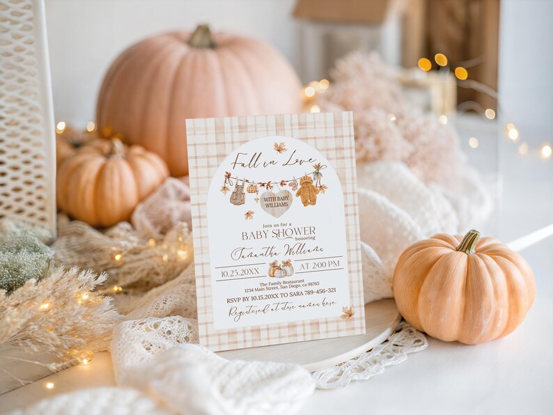 May include: A baby shower invitation with a fall theme. The invitation features a plaid background and the words "Fall in Love" at the top. The invitation includes the date, time, and honoree's name. Pumpkins and decorative elements surround the invitation.