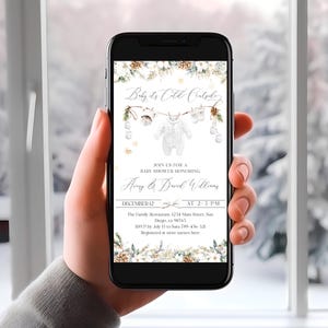 May include: A smartphone screen shows a baby shower invitation with the words "Baby it's Cold Outside." The design includes baby clothes, snowflakes, and pinecones. The invitation is for Amy & David Williams on December 12. The time is 2-3 PM.