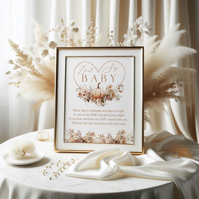 Pu&ograve; includere: Un cartello incorniciato con la scritta "Don't Say BABY" in elegante calligrafia, con un design floreale a forma di cuore con una zucca. Il cartello include le istruzioni per un gioco per il baby shower. La cornice &egrave; dorata e lo sfondo &egrave; di colore neutro.