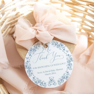 May include: A round thank you tag with a blue floral border and a teddy bear illustration. The tag says "Thank you for showering us with love! Avery & David Baby Shower March 20xx".