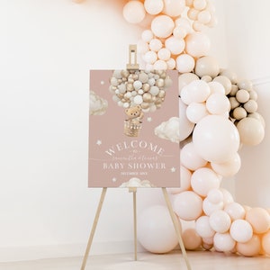 Pode incluir: Uma placa de boas-vindas rosa com um urso de pelúcia em um balão de ar quente feito de balões dourados e brancos. A placa diz "Bem-vindos a Samantha & Thomas Baby Shower Dezembro 20XX".