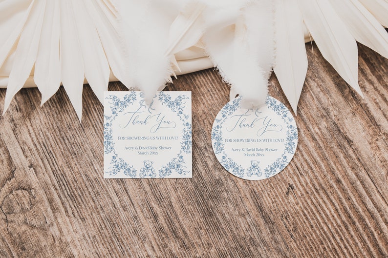 May include: Two blue and white thank you tags with a floral border and a teddy bear design. The text on the tags reads "Thank You for showering us with love! Avery & David Baby Shower March 20xx".