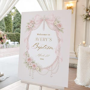 Peut inclure: Panneau blanc sur chevalet avec l'inscription "Welcome to Avery's Baptism" en lettres dorées. Le panneau est orné de roses roses, de perles et de rubans. La date "March 27, 20XX" est également affichée. Le panneau est installé lors d'un événement.