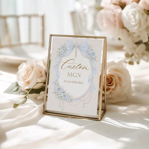 May include: A gold-framed sign with the words "Custom Sign" in elegant script, surrounded by light blue floral and ribbon accents. The sign is fully editable and suitable for weddings or special events.