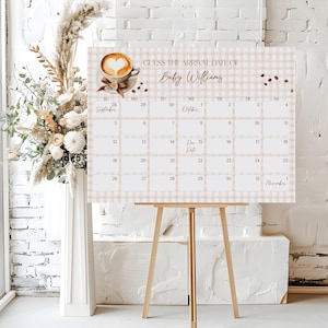 May include: A baby shower calendar with a beige gingham pattern and the text "GUESS THE ARRIVAL DATE OF Baby Williams." The calendar features a coffee cup graphic and a wooden easel stand. The calendar displays the months of September and October.