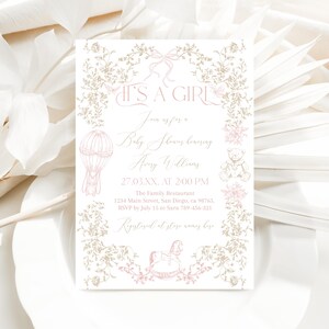 Op de afbeelding: Een uitnodiging voor een babyshower met de tekst "IT'S A GIRL" in elegant schrift. De uitnodiging heeft een roze en gouden bloemenontwerp, een illustratie van een luchtballon en een illustratie van een schommelpaard. De details omvatten de datum, tijd en locatie.