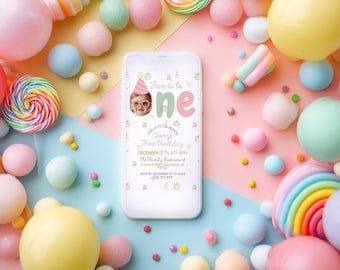 May include: A smartphone displays a first birthday invitation with the text "Fun to be one." The invitation features a photo of a baby wearing glasses and a party hat, surrounded by colorful candies and balloons.