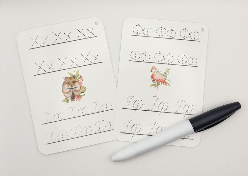 May include: Two white dry-erase boards with dotted lines for practicing handwriting. One board features a hamster illustration and the other features a flamingo illustration. The boards have holes in the top corner for hanging. A black and white dry-erase marker is included.