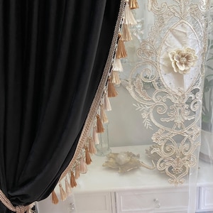 Pu&ograve; includere: Tenda in velluto nero con finiture decorative e nappe. A destra &egrave; visibile una tenda trasparente con un motivo floreale ricamato. Le tende sono adatte per un soggiorno o una camera da letto.