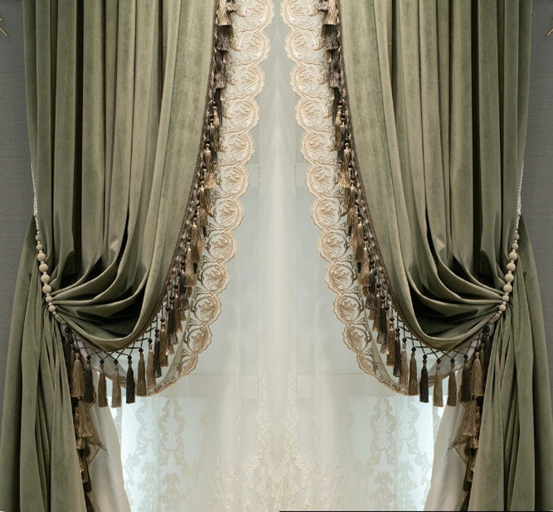 May include: Olive green velvet curtains with decorative trim and tassels. The curtains are draped and held with beaded tiebacks. A sheer, embroidered panel is visible behind the curtains, adding a layer of elegance to the window treatment.