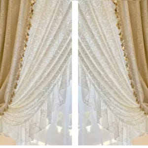 May include: Elegant cream-colored curtains with intricate floral patterns. The curtains are draped in a layered design, with a sheer white underlayer. Gold-colored tassels adorn the edges, adding a touch of luxury. The curtains are a decorative window treatment.