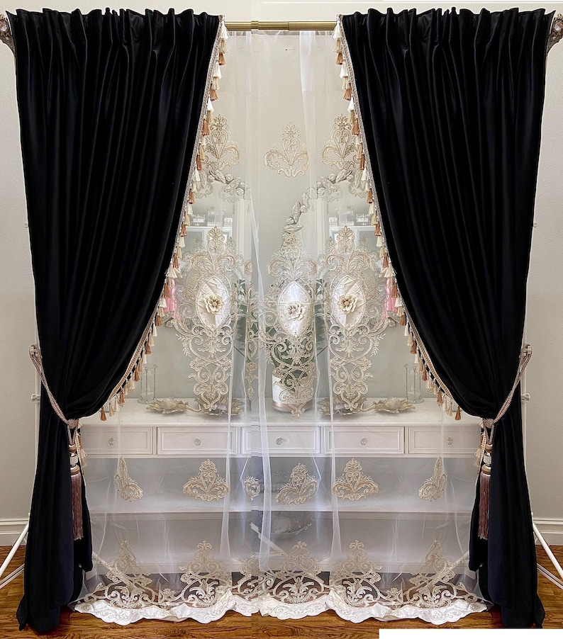 Pu&ograve; includere: Eleganti tende in velluto nero con fermatende a nappe dorate incorniciano una tenda bianca trasparente con ricami dorati. Le tende sono appese a un'asta dorata, creando un aspetto lussuoso e sofisticato.