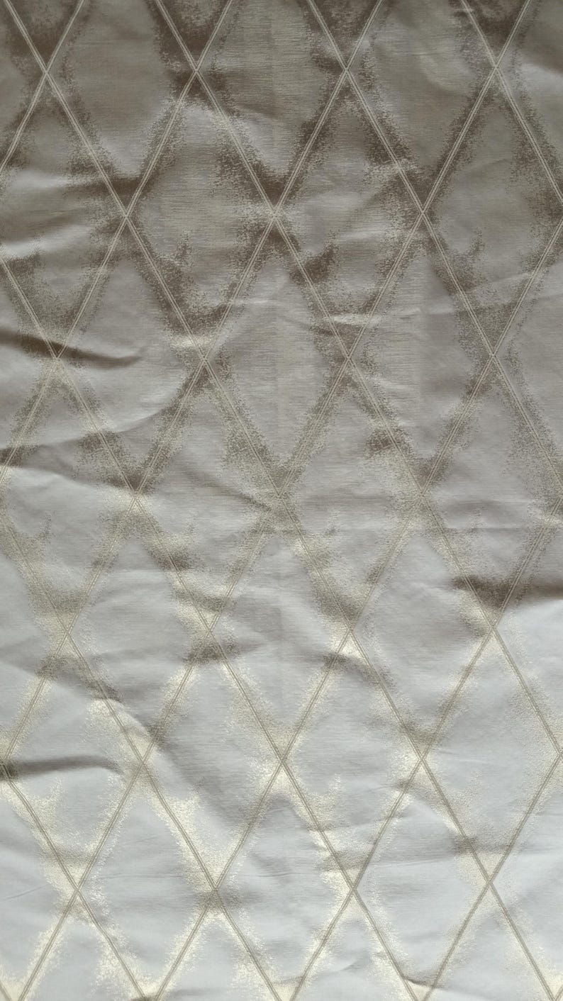 May include: A close-up of a fabric with a diamond pattern. The fabric is a light beige color with a subtle sheen. The diamond pattern is created with a lighter, textured beige thread, adding depth and visual interest to the textile.