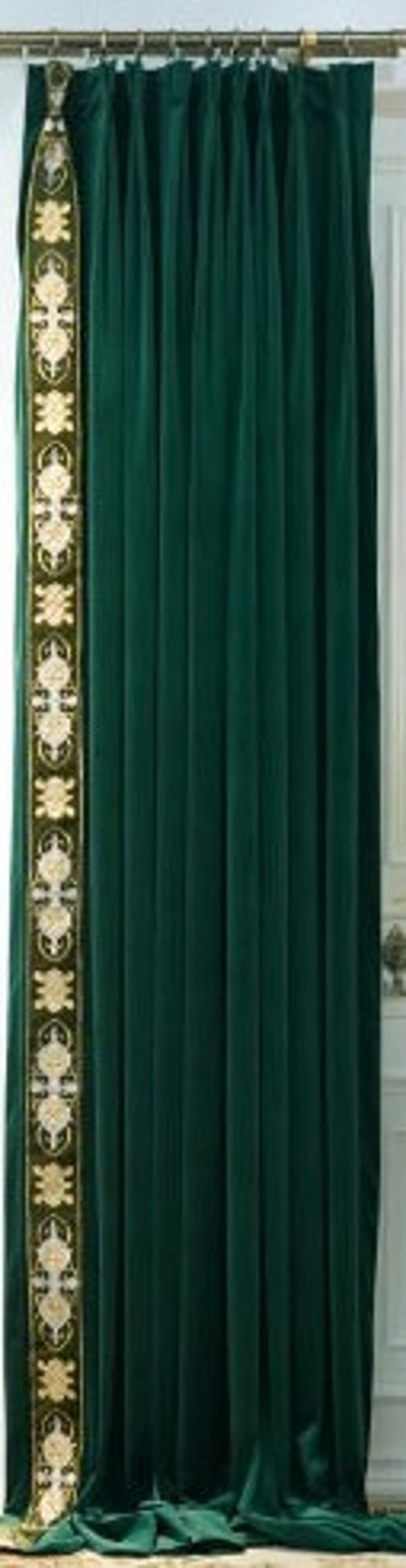 May include: Dark green velvet curtain with a decorative border. The border has an ornate design in gold and olive green. The curtain hangs from a gold rod. The curtain is partially drawn, revealing a white door frame.