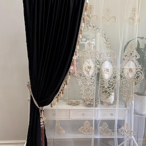 Pu&ograve; includere: Elegante tenda in velluto nero abbinata a una tenda bianca trasparente con ricami dorati ornati. Le tende sono decorate con nappe decorative e sono progettate per uno stile di arredamento sofisticato.